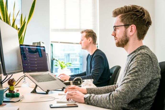 Mann sitzt auf einem Stuhl, trägt ein graues Rundhals-Langarmshirt und benutzt eine Apple Magic Keyboard
